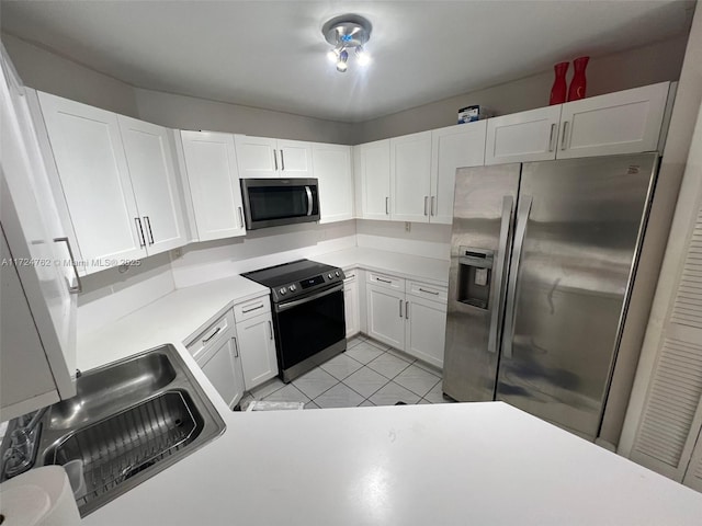 kitchen with light countertops, appliances with stainless steel finishes, white cabinets, a sink, and light tile patterned flooring