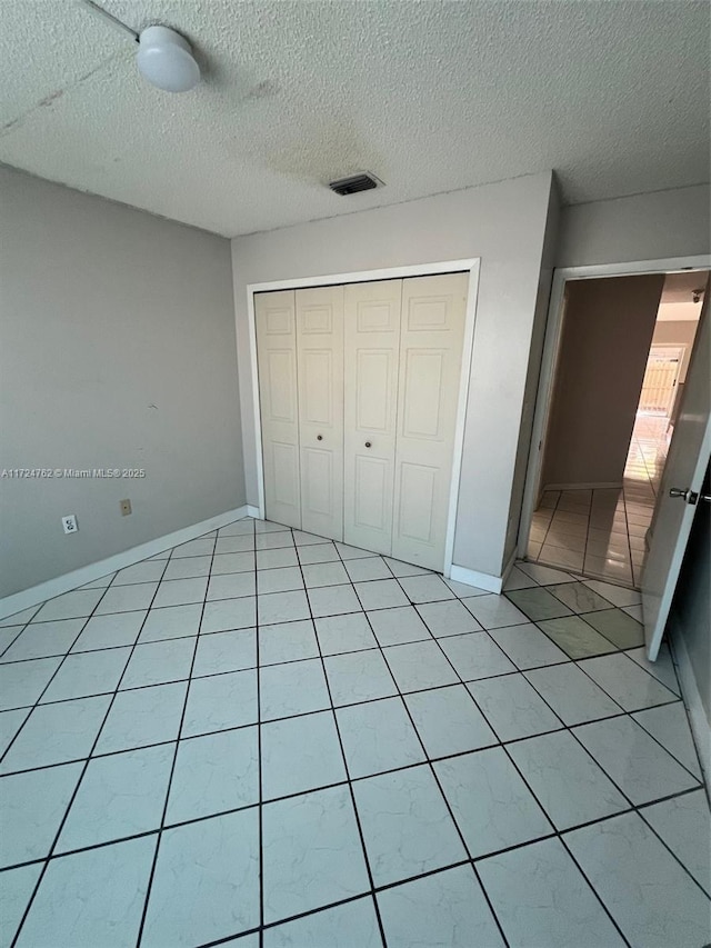 unfurnished bedroom with light tile patterned floors, a closet, visible vents, a textured ceiling, and baseboards