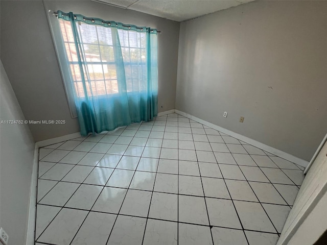 empty room featuring baseboards and light tile patterned flooring