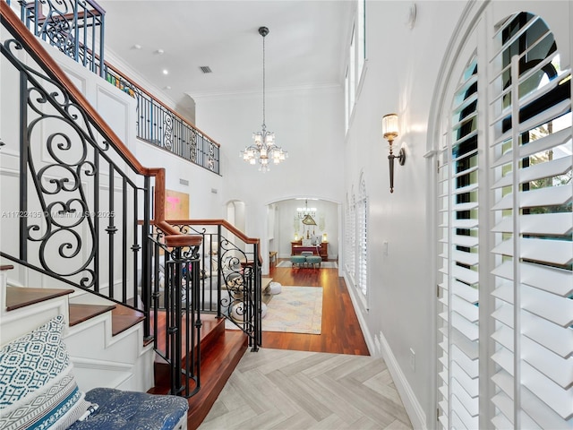 stairs with a towering ceiling, an inviting chandelier, parquet floors, and crown molding