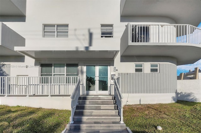 view of exterior entry with french doors, a balcony, and stucco siding