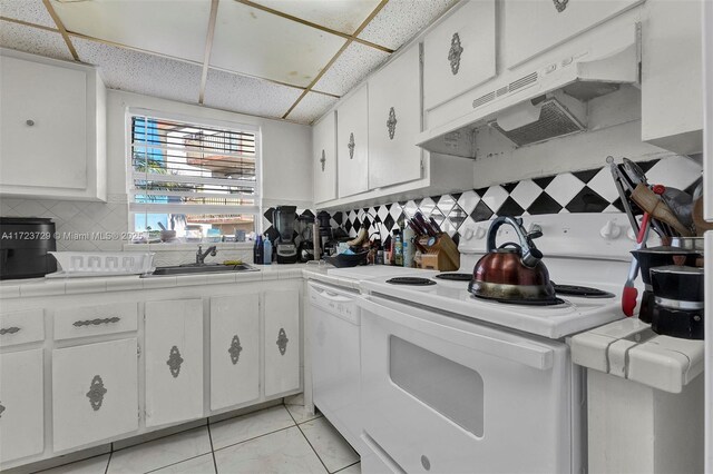 kitchen with tile countertops, a paneled ceiling, a sink, under cabinet range hood, and white appliances