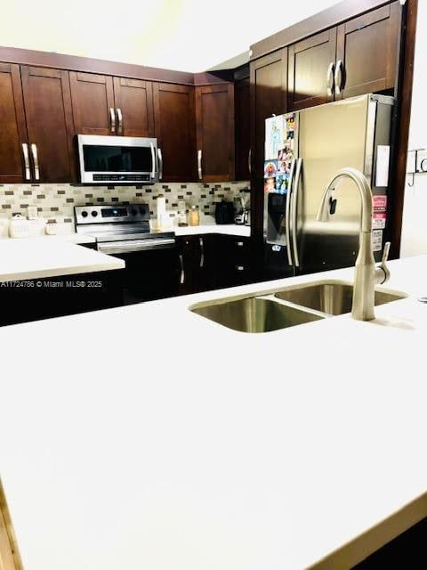 kitchen with dark brown cabinets, backsplash, light countertops, appliances with stainless steel finishes, and a sink