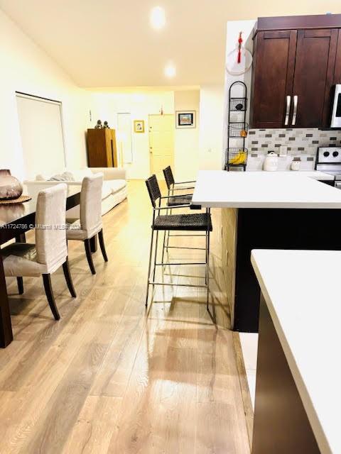 kitchen featuring a peninsula, light wood-style flooring, light countertops, a kitchen breakfast bar, and backsplash