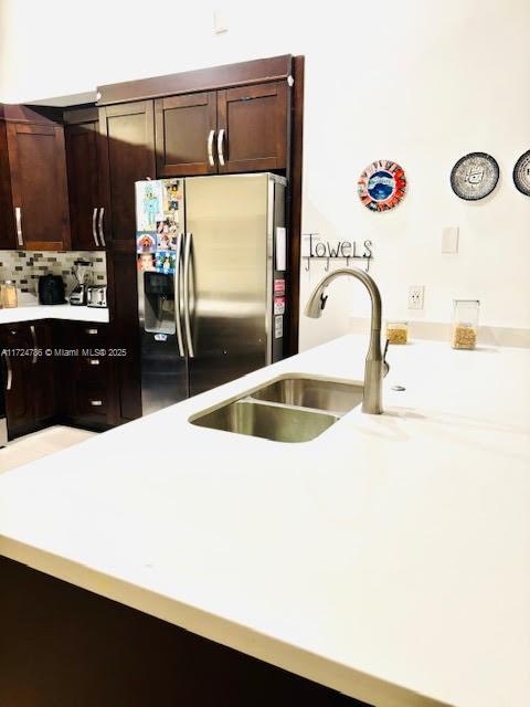 kitchen with a sink, stainless steel fridge, dark brown cabinetry, and light countertops