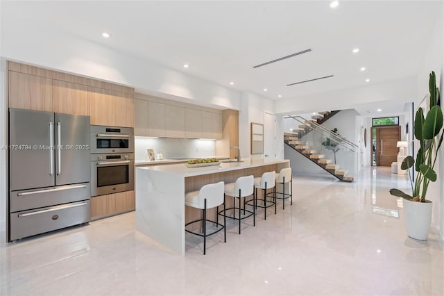 kitchen with light brown cabinets, a kitchen island with sink, a kitchen breakfast bar, sink, and stainless steel appliances