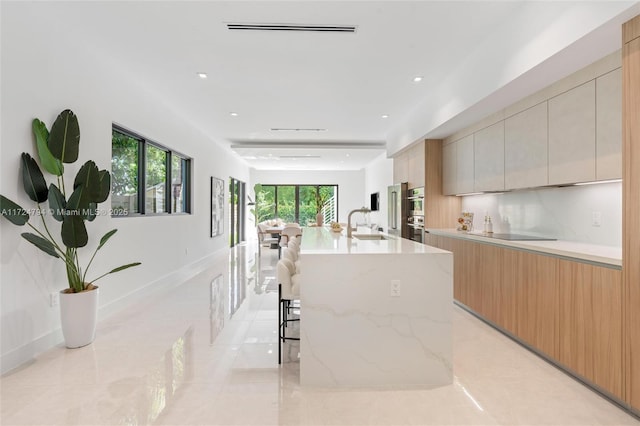 kitchen featuring a spacious island, a kitchen bar, sink, and light brown cabinetry