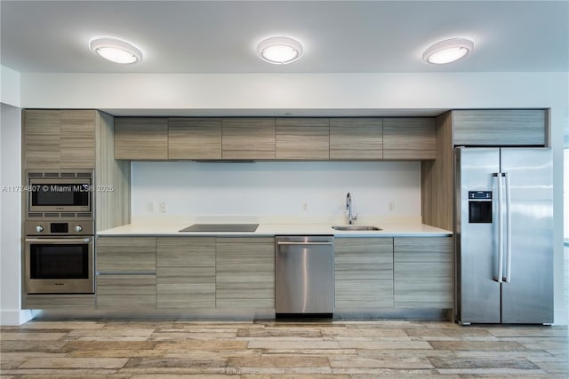 kitchen featuring stainless steel appliances, light countertops, light wood-style flooring, a sink, and modern cabinets