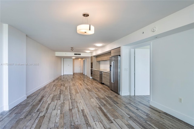 kitchen with stainless steel refrigerator with ice dispenser, light wood finished floors, visible vents, light countertops, and baseboards