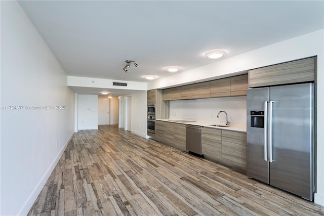 kitchen featuring light wood finished floors, stainless steel appliances, light countertops, a sink, and modern cabinets