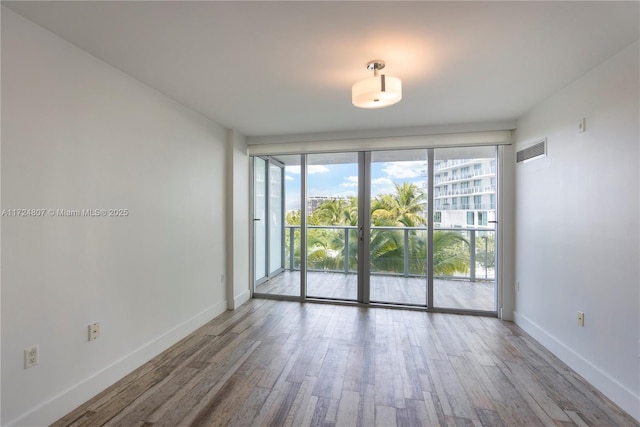 empty room with expansive windows, visible vents, baseboards, and wood finished floors