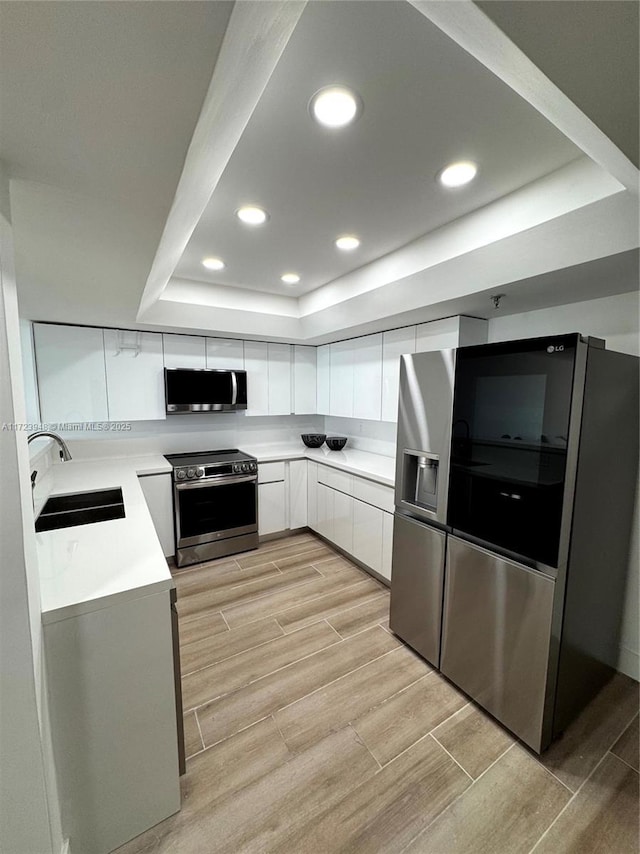 kitchen featuring a raised ceiling, white cabinetry, sink, and appliances with stainless steel finishes