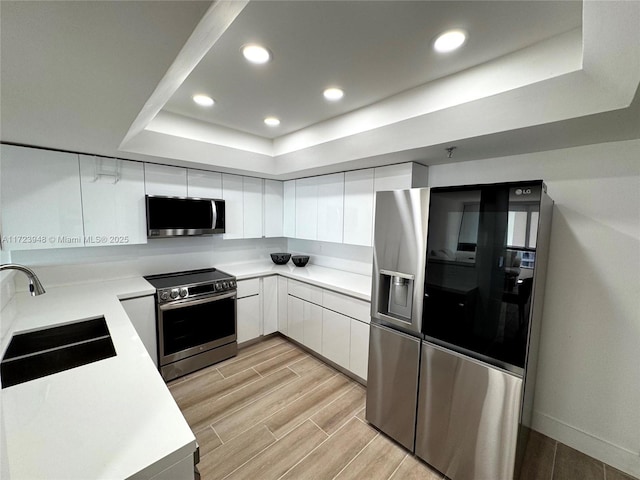 kitchen with a raised ceiling, white cabinetry, sink, and appliances with stainless steel finishes