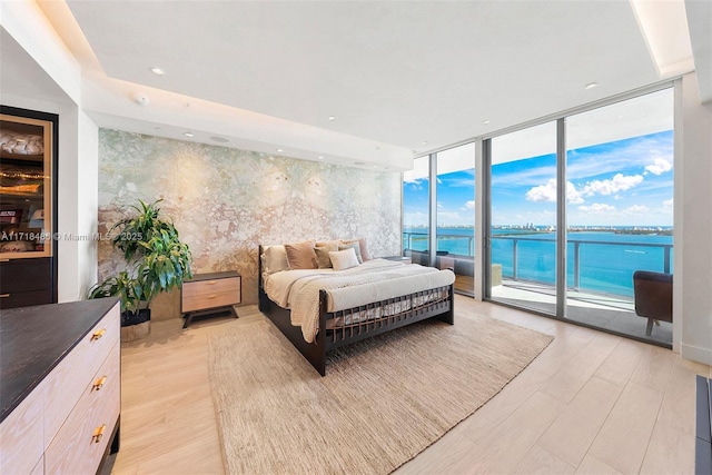 bedroom featuring access to exterior, a water view, multiple windows, and floor to ceiling windows