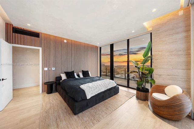 bedroom with light wood-type flooring, access to outside, a wall of windows, and wooden walls