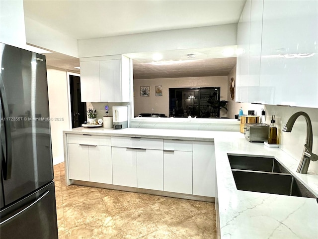 kitchen with sink, white cabinets, black refrigerator, and kitchen peninsula