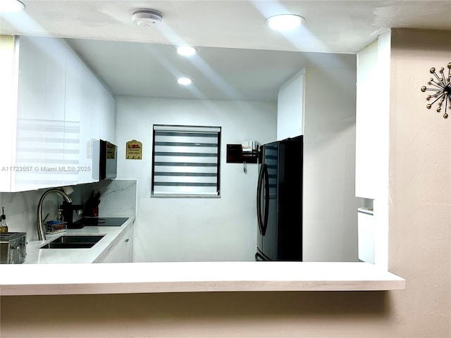 kitchen with sink, black fridge, white cabinetry, and tasteful backsplash