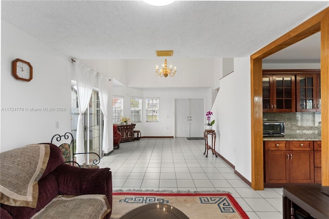 interior space with light tile patterned floors, visible vents, an inviting chandelier, a textured ceiling, and baseboards