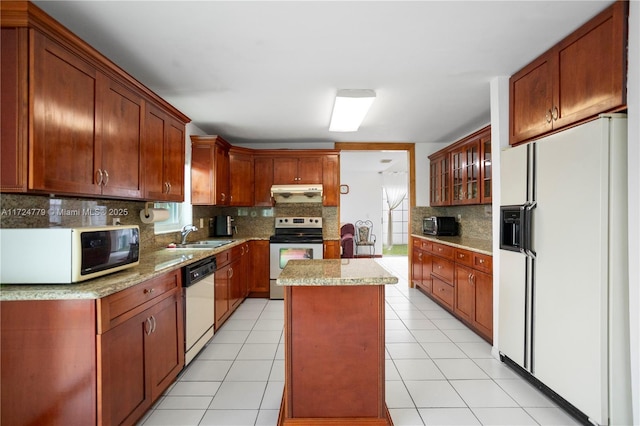 kitchen with white appliances, backsplash, a center island, under cabinet range hood, and a sink