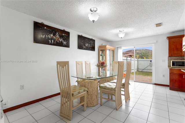 dining space featuring visible vents, a textured ceiling, baseboards, and light tile patterned floors