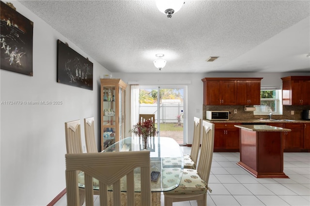 kitchen with reddish brown cabinets, a center island, decorative backsplash, white microwave, and a sink