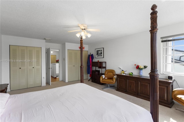 bedroom featuring a textured ceiling, ceiling fan, light carpet, visible vents, and two closets