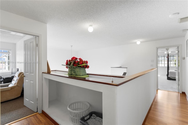 hallway featuring visible vents, plenty of natural light, a textured ceiling, and wood finished floors