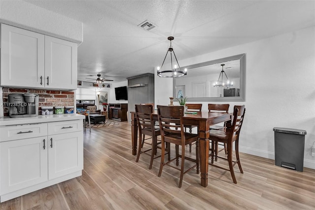 dining space with a textured ceiling, light hardwood / wood-style flooring, and ceiling fan with notable chandelier