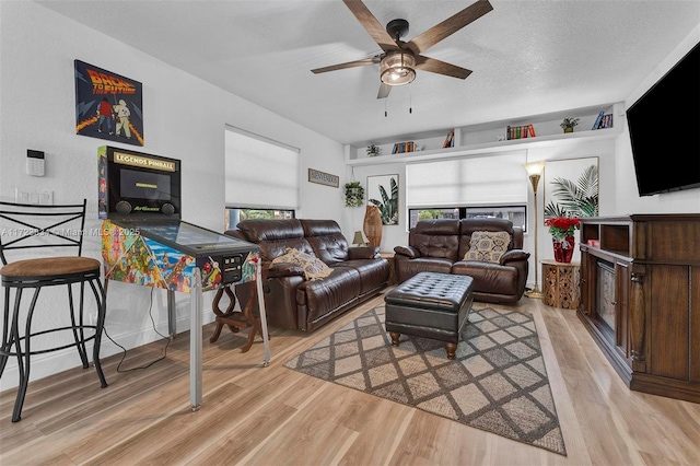 living room featuring ceiling fan, light wood-type flooring, and a textured ceiling