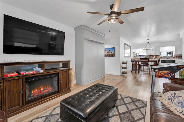 living room with a textured ceiling, ceiling fan with notable chandelier, and light wood-type flooring