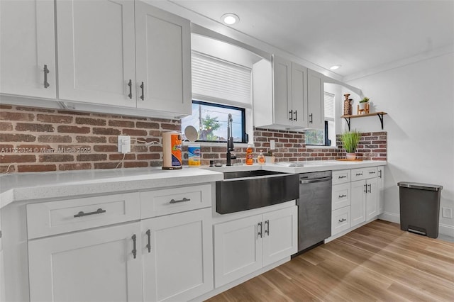 kitchen with white cabinetry, sink, stainless steel dishwasher, crown molding, and light wood-type flooring