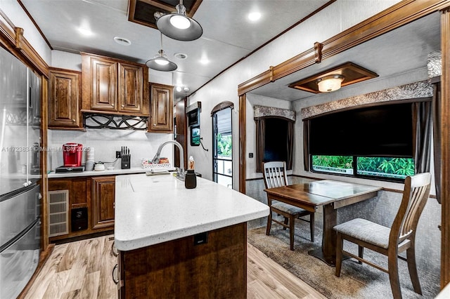 kitchen featuring light wood-type flooring, tasteful backsplash, crown molding, a center island with sink, and stainless steel refrigerator