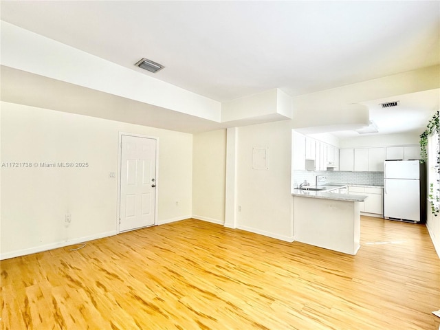 kitchen with light wood finished floors, visible vents, backsplash, a peninsula, and freestanding refrigerator