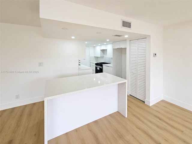 kitchen with a center island, black gas range oven, light stone counters, light hardwood / wood-style floors, and white cabinets