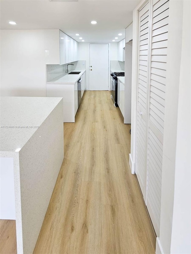 kitchen with black gas range, sink, stainless steel dishwasher, light hardwood / wood-style floors, and white cabinets