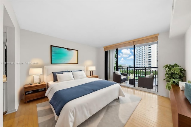 bedroom with access to outside, a wall of windows, and light hardwood / wood-style flooring