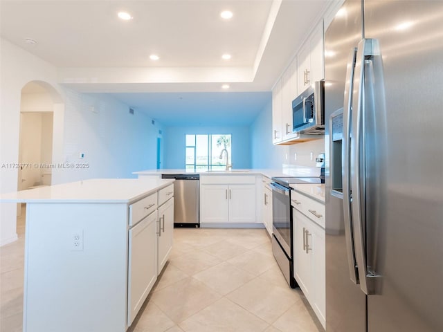 kitchen with sink, kitchen peninsula, appliances with stainless steel finishes, a kitchen island, and white cabinetry