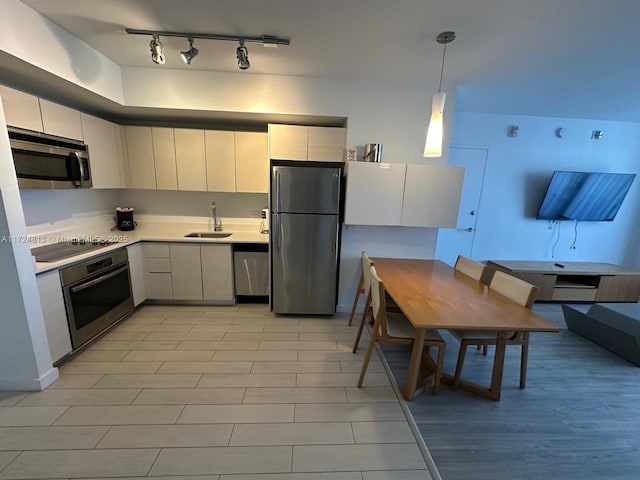 kitchen with a sink, white cabinets, light countertops, appliances with stainless steel finishes, and decorative light fixtures