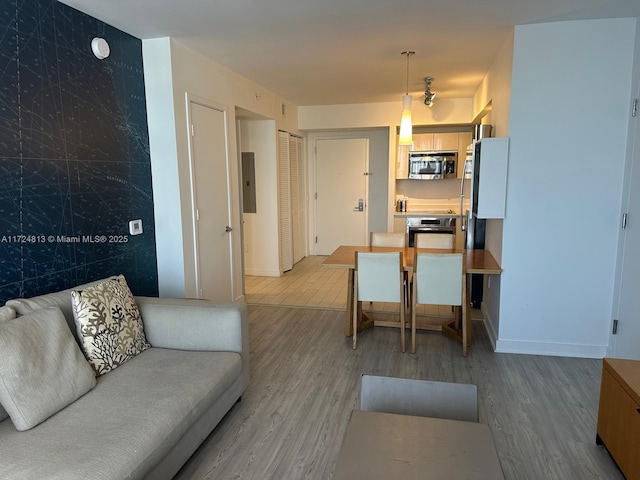 living area with baseboards, electric panel, and light wood-style floors