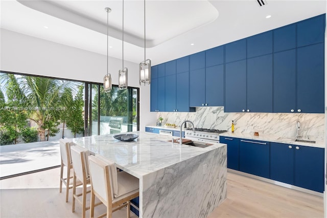 kitchen featuring sink, a breakfast bar, decorative light fixtures, a raised ceiling, and a large island with sink