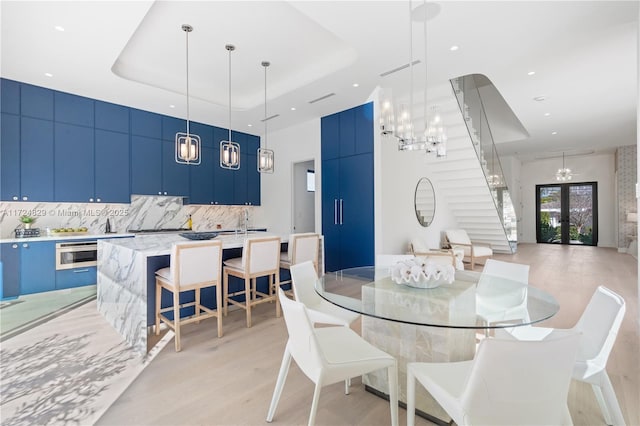 dining area featuring french doors, a raised ceiling, sink, and light hardwood / wood-style flooring