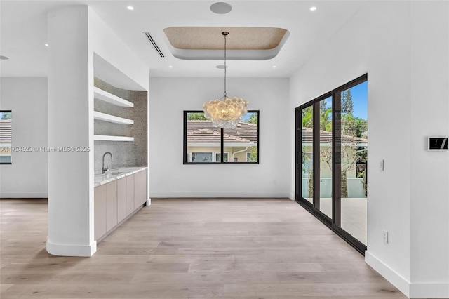 interior space with light wood-type flooring, a raised ceiling, a notable chandelier, and sink