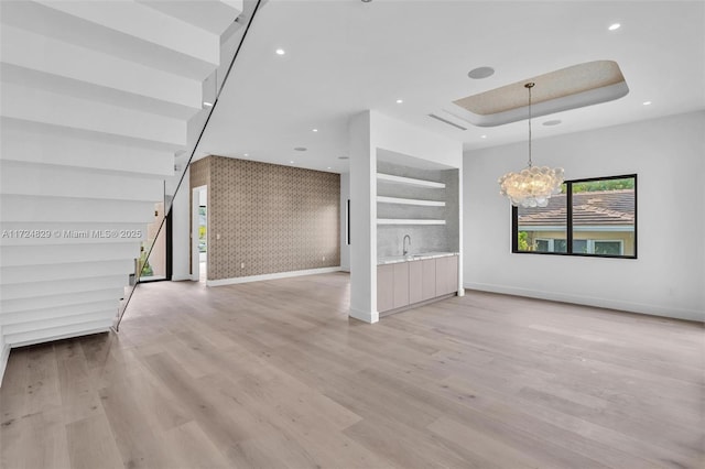 unfurnished living room featuring a tray ceiling, light wood-type flooring, and a notable chandelier