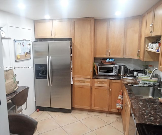 kitchen featuring dark stone countertops, stainless steel fridge, sink, and light tile patterned flooring