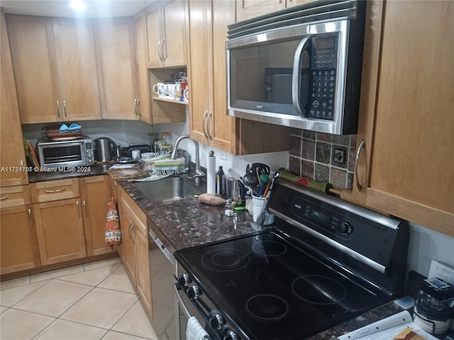 kitchen featuring dark stone countertops, light tile patterned flooring, sink, and stainless steel appliances