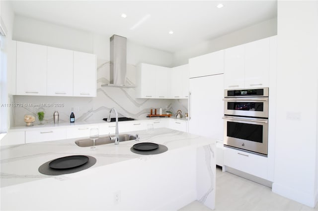 kitchen featuring stainless steel double oven, ventilation hood, light stone countertops, and white cabinets