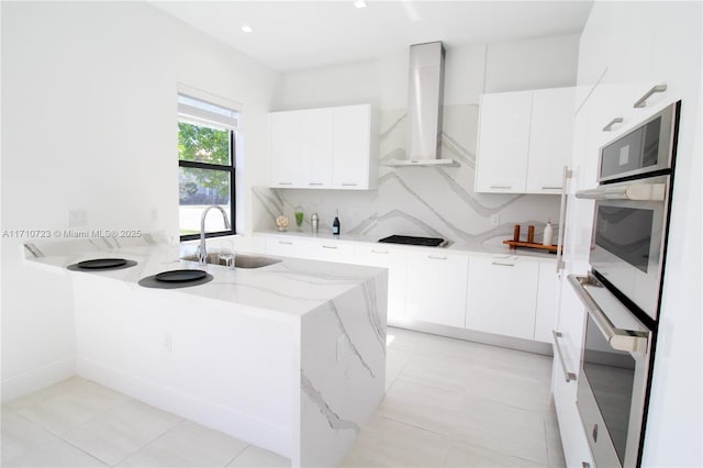 kitchen with white cabinetry, wall chimney range hood, and sink