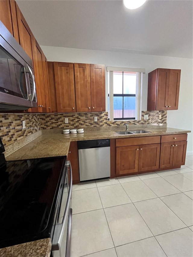 kitchen featuring sink, light tile patterned floors, appliances with stainless steel finishes, decorative backsplash, and dark stone counters