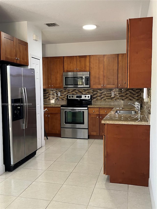 kitchen with appliances with stainless steel finishes, tasteful backsplash, sink, dark stone counters, and light tile patterned floors