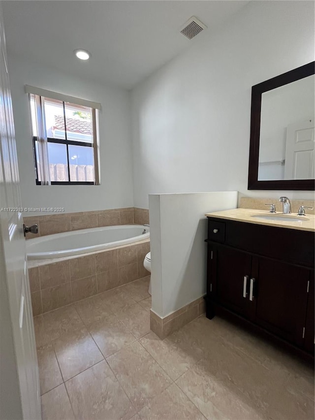 bathroom featuring vanity, a relaxing tiled tub, tile patterned floors, and toilet